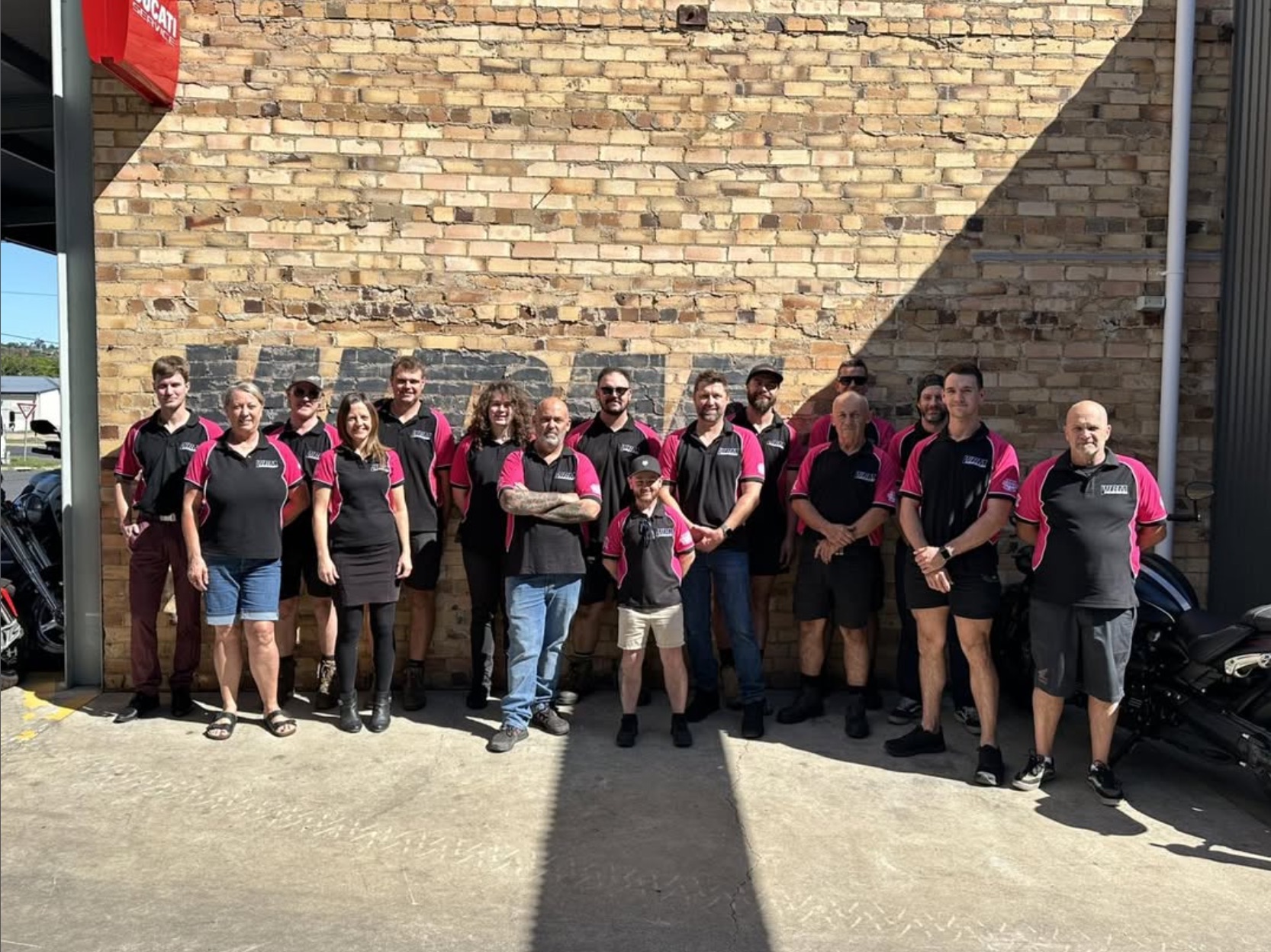 Team wearing pink and black shirts outside their workshop