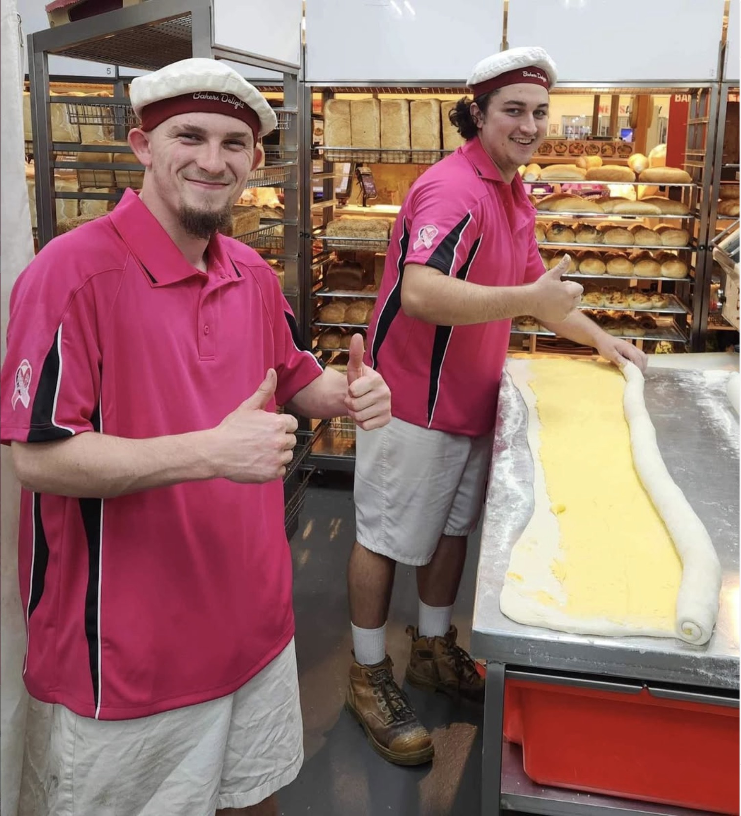 Two bakers in pink shirts giving thumbs up in the bakery